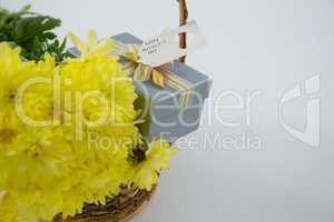 Gift box and bunch of yellow flowers in wicker basket with happy mothers day tag