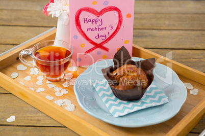 Cupcake, tea, flower vase and happy mothers day greetings card in tray