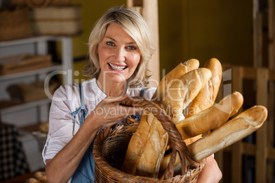 Female staff holding basket of baguettes in bakery section