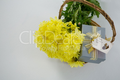 Gift box and bunch of yellow flowers in wicker basket with happy mothers day tag