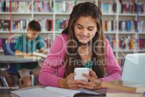 Smiling schoolgirl using mobile phone in library