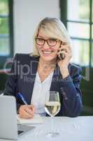 Businesswoman talking on mobile phone while writing on diary