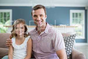 Smiling father and daughter sitting on sofa in living room at home