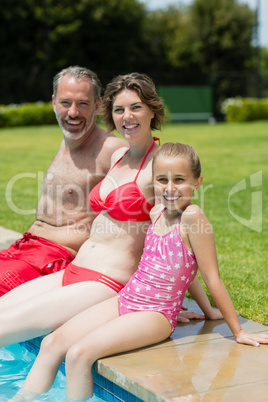 Portrait of parents and daughter sitting on poolside in pool water