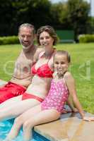 Portrait of parents and daughter sitting on poolside in pool water