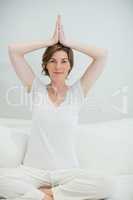 Smiling woman doing yoga exercise on bed in bedroom at home