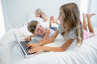 Girl and boy using laptop on bed in bedroom at home