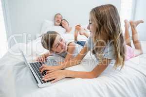 Girl and boy using laptop on bed in bedroom at home