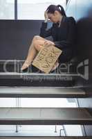 Depressed businesswoman sitting on stairs holding cardboard sheet with text need work