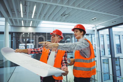 Male architects discussing over blueprint in corridor