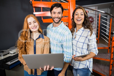 Portrait of happy executives holding laptop and digital tablet