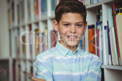 Portrait of smiling schoolboy standing with arms crossed in library