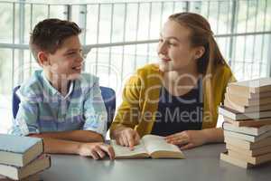 Smiling school kids reading books in library at school