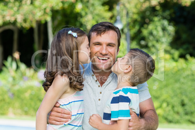 Portrait of father receiving kisses from son and daughter