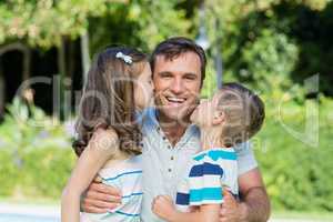 Portrait of father receiving kisses from son and daughter