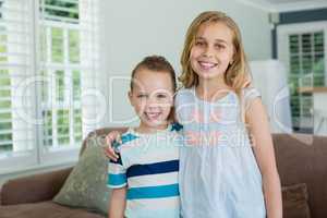 Portrait of smiling sister and brother standing with arms around in living room