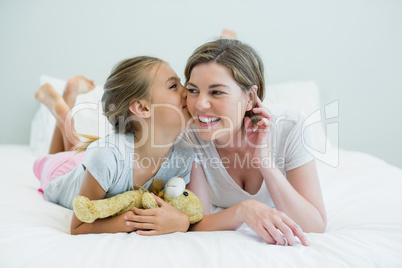 Adorable girl kissing her mother lying on a bed