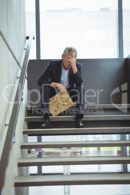 Depressed businessman sitting on stairs holding cardboard sheet with text need work