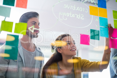 Smiling executives writing on sticky notes on glass wall