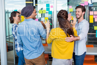 Smiling executives giving high five while discussing over sticky notes