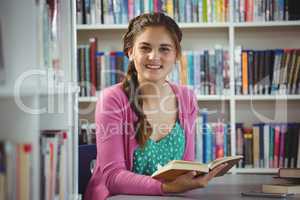 Portrait of smiling schoolgirl reading book in library