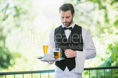 Male waiter holding tray with beer glass and coffee cup in restaurant