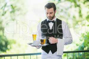 Male waiter holding tray with beer glass and coffee cup in restaurant