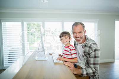 Smiling father and son working on computer at home