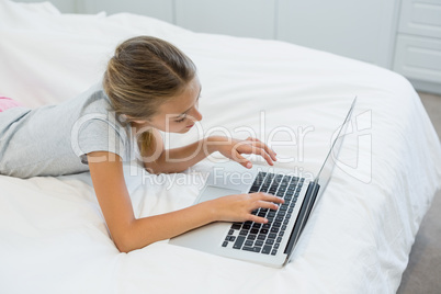 Girl lying on bed and using laptop in bedroom