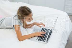 Girl lying on bed and using laptop in bedroom