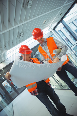 Male architects discussing over blueprint in corridor