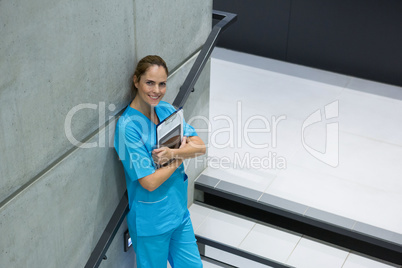 Portrait of female surgeon holding clipboard and digital tablet on staircase