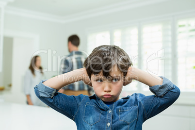 Boy covers his ears with his hands while parents arguing in background