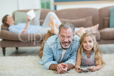 Happy father and daughter using mobile phone while lying on floor in living room