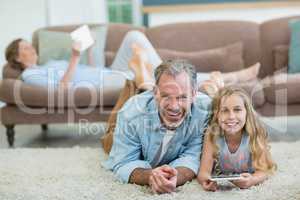 Happy father and daughter using mobile phone while lying on floor in living room