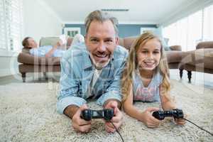 Happy father and daughter playing video game while lying on floor in living room