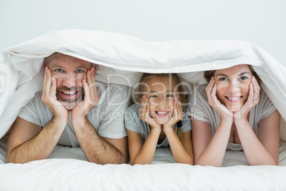 Happy family lying under blanket on bed at home