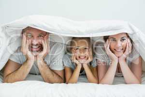 Happy family lying under blanket on bed at home