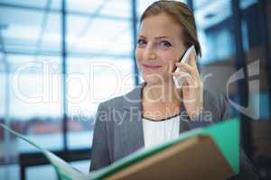 Businesswoman talking on mobile phone while holding files