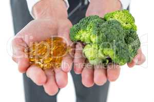 Businessman holding broccoli and vitamin pills