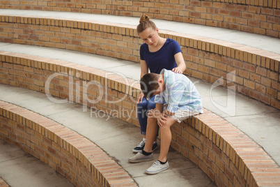 Schoolgirl consoling her sad friend on steps in campus