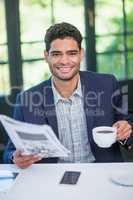 Happy businessman holding coffee cup and newspaper