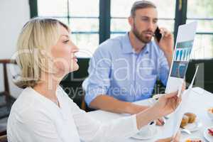 Female executive looking at document while colleague talking on mobile phone