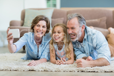 Family taking selfie from mobile phone while lying together on carpet in living room