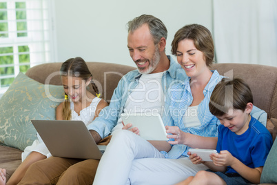 Happy family using mobile phone, digital tablet and laptop in living room