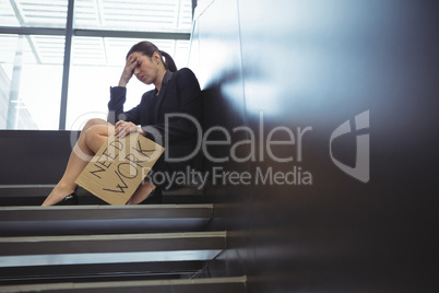 Depressed businesswoman sitting on stairs holding cardboard sheet with text need work