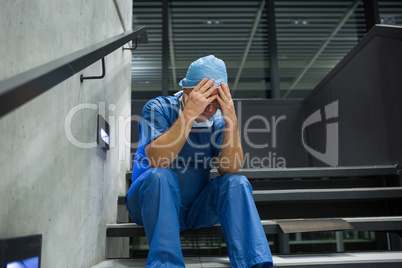 Tensed male surgeon sitting with hands on forehead on staircase