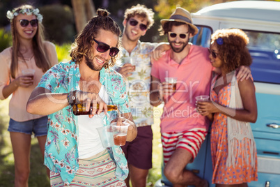 Happy man pouring beer in a glass while his friends standing in background