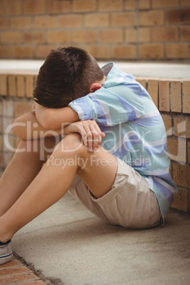 Sad schoolboy sitting alone on steps in campus