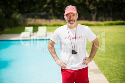 Portrait of swim coach with stopwatch standing with hands on hip near poolside